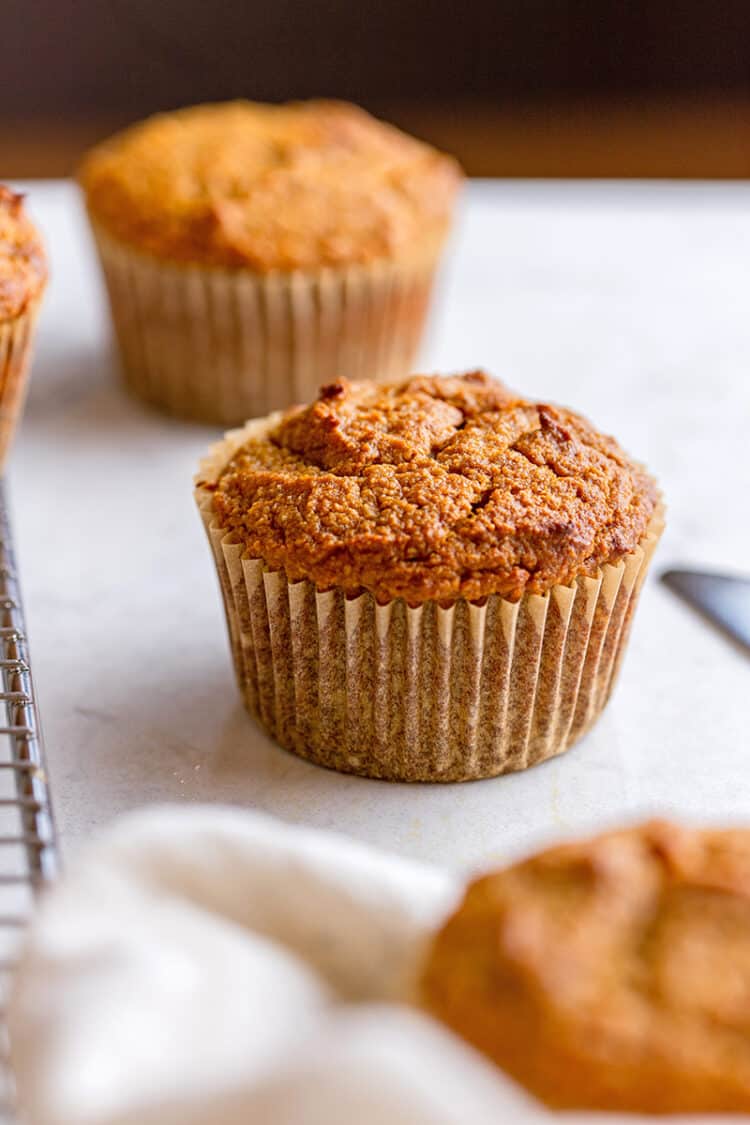 Three paleo pumpkin muffins are on a marble counter top.