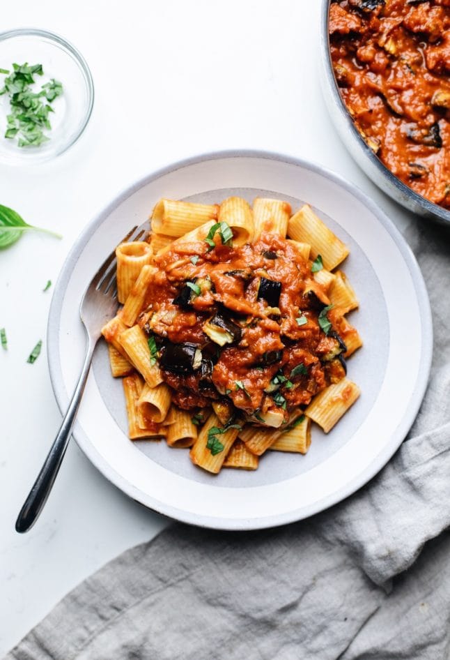 A ceramic bowl with eggplant pasta with a fork in it with a gray napkin on the side.