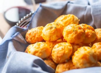 Basket of cheese puffs with glasses of wine in the background.