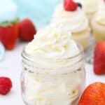 A small glass jar filled with beautifully piped frosting. The jar is surrounded by berries