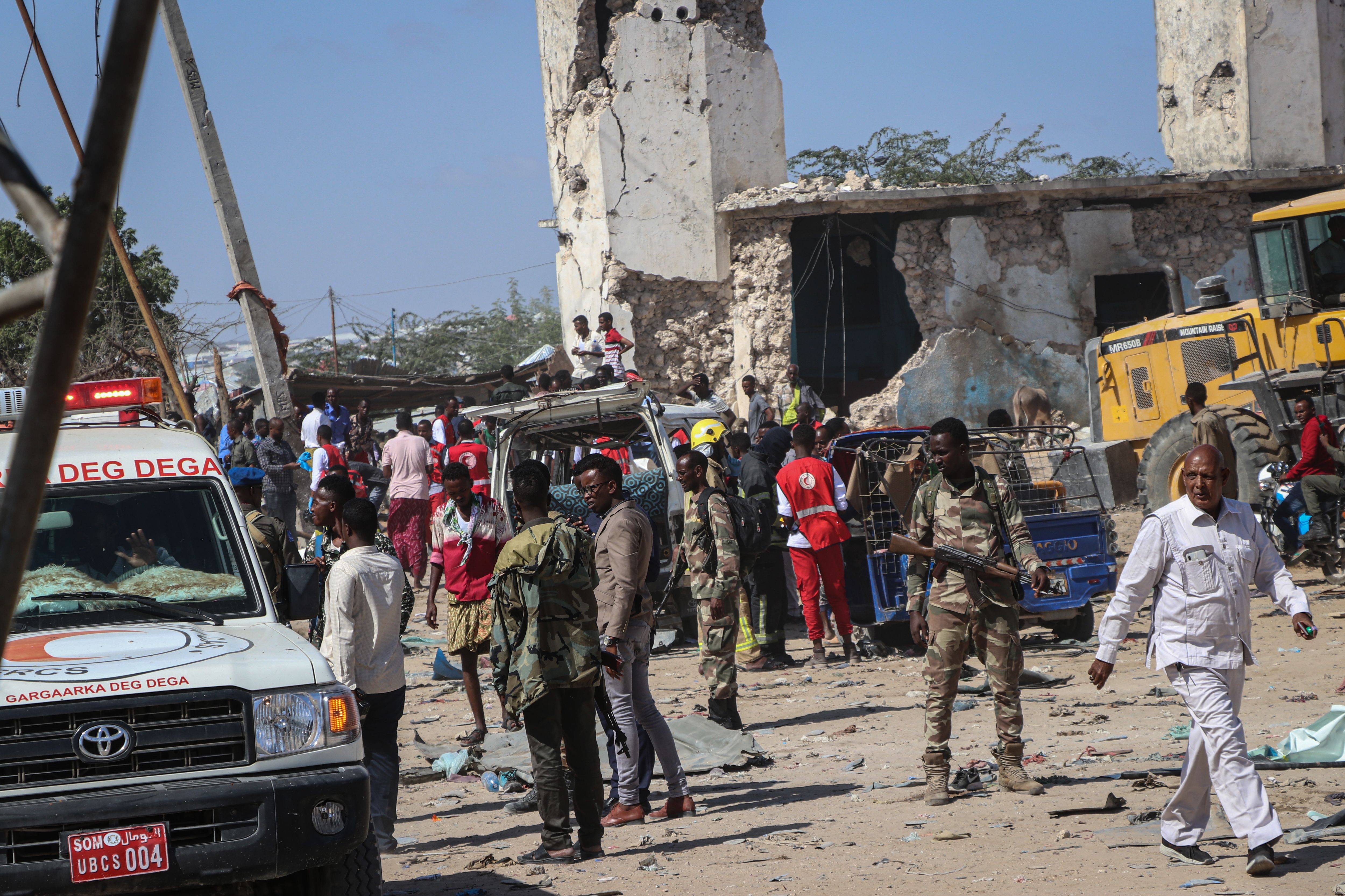 Soldiers and emergency vehicles in the site of the blast; damaged vehicles and buildings can be seen in the background.