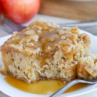 A slice of apple cake on a white plate topped with caramel sauce.
