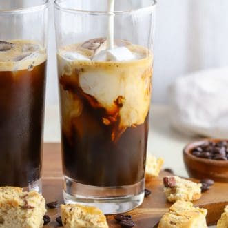 Two glasses of iced coffee with cream being poured in.