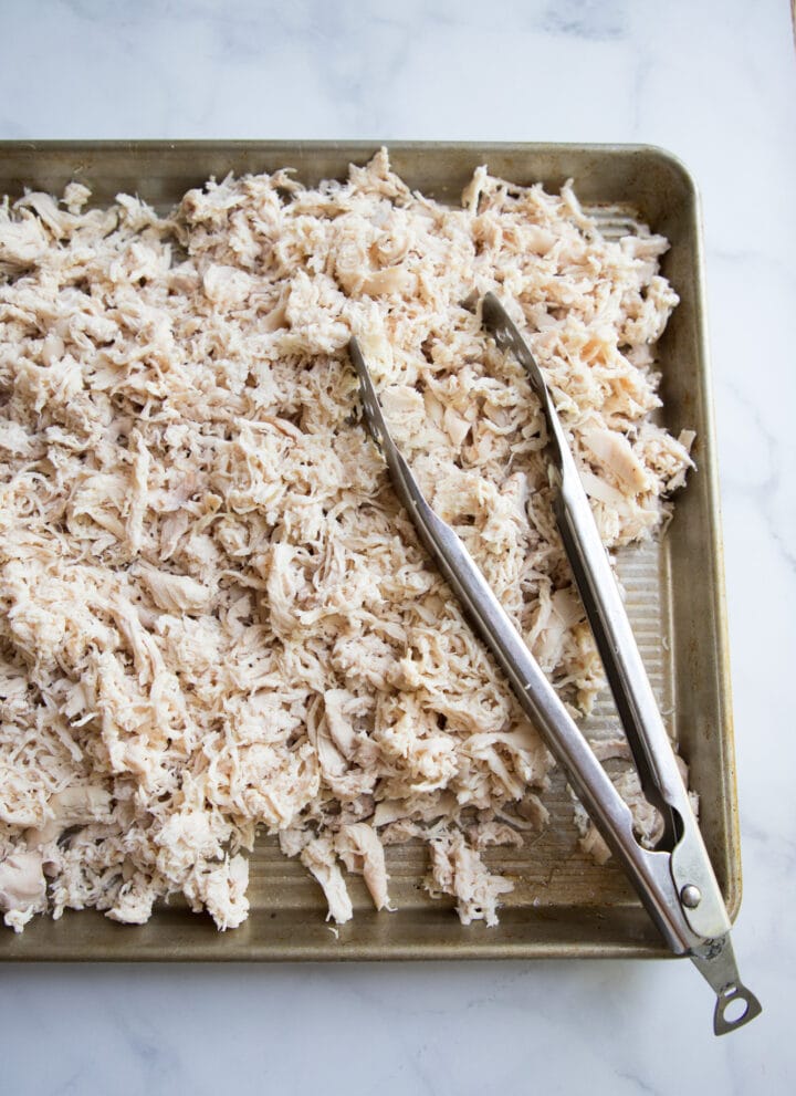 a large cookie sheet of shredded chicken with tongs