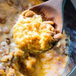 Wooden Spoon scooping up sweet potato casserole with a sweet brown sugar pecan topping.