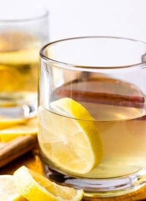 Hot Toddy with honey and Lemon in a glass mug garnished with a cinnamon stick.