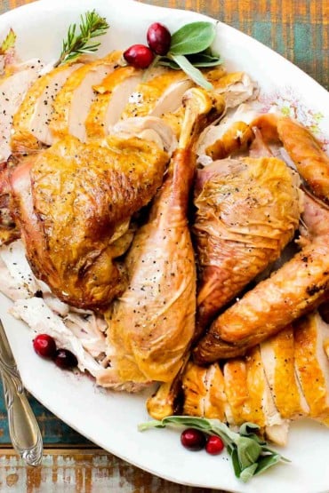 A large white platter of cooked and carved spatchcocked turkey with cranberries next to it.