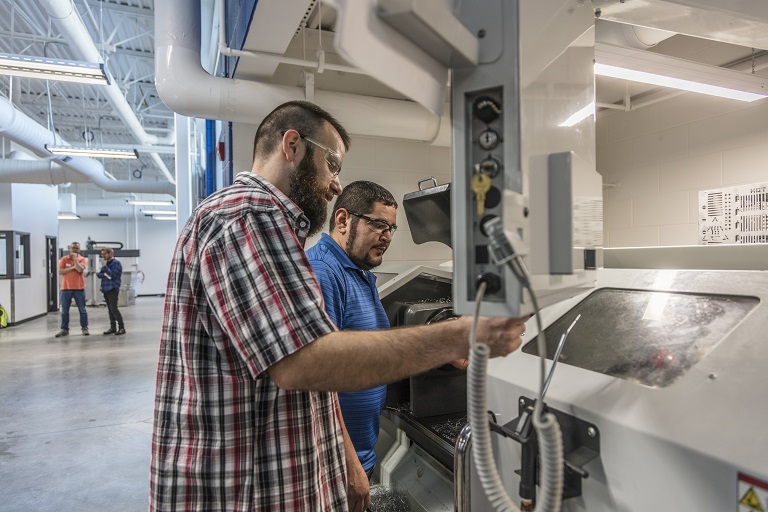 two older male students working on a computerized manufacturing machine
