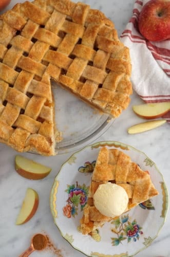 A top town photo of an apple pie with a lattice top and a piece on a plate.