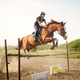 Young female jockey on horse leaping over hurdle