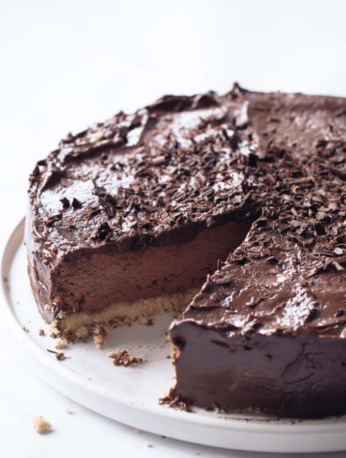 a keto chocolate cheesecake with chocolate flakes on a white serving platter