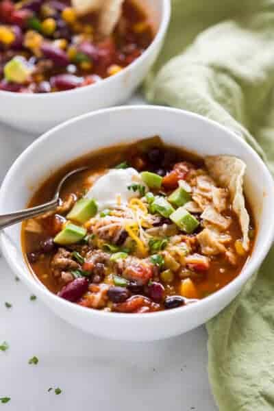 Taco soup in a bowl with a spoon, garnished with avocado, sour cream and chips.