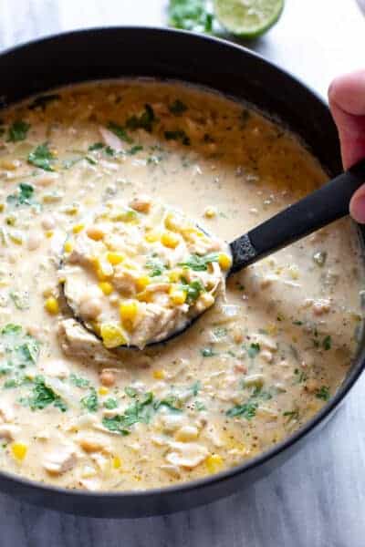 A ladle spooning white chicken chili soup from a soup pot.
