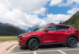 Chef Dennis behind a Soul Red Mazda CX-5 with the Rocky Mountains in the background