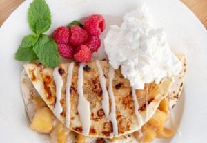 apple pie fold-over on a white plate with raspberries and whipped cream
