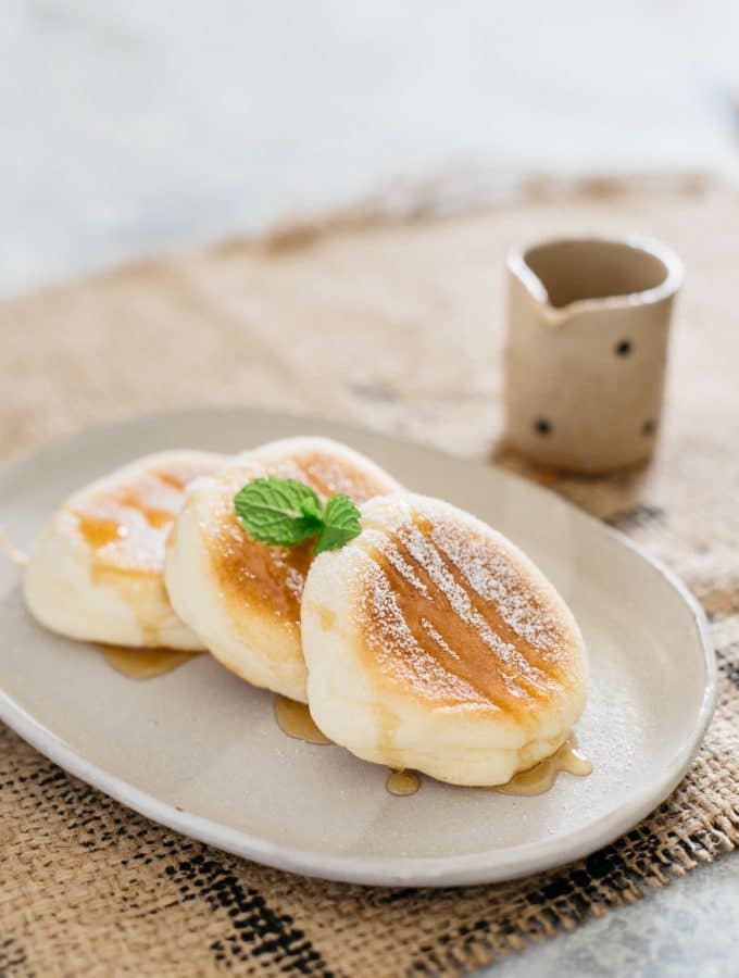 three souffle pancake served on an oval plate dusted with icing sugar and syrup