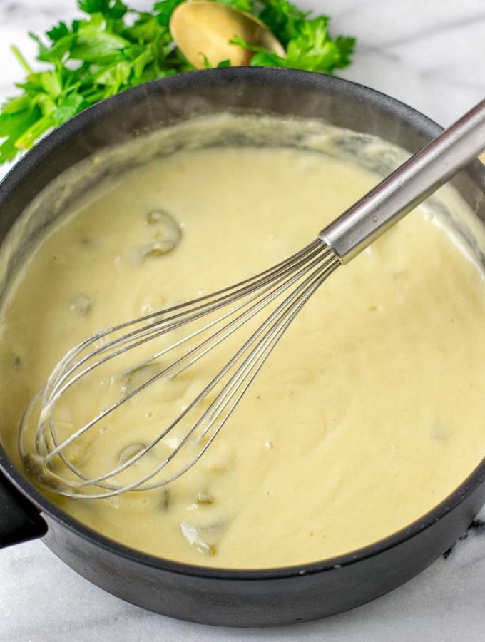 Ready White Enchilada Sauce with a wire whisk in the pot.