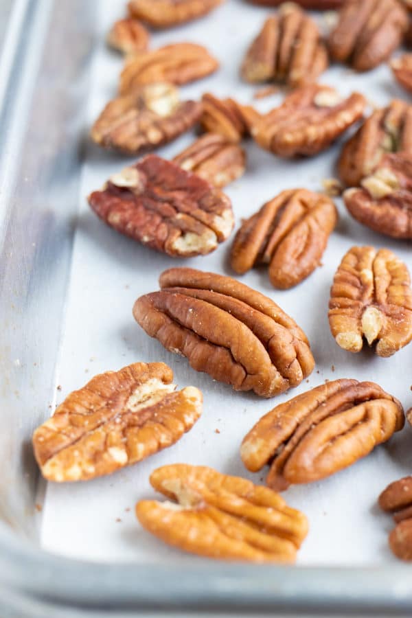 Toasted pecans on a large baking sheet that are going to be roasted in the oven.