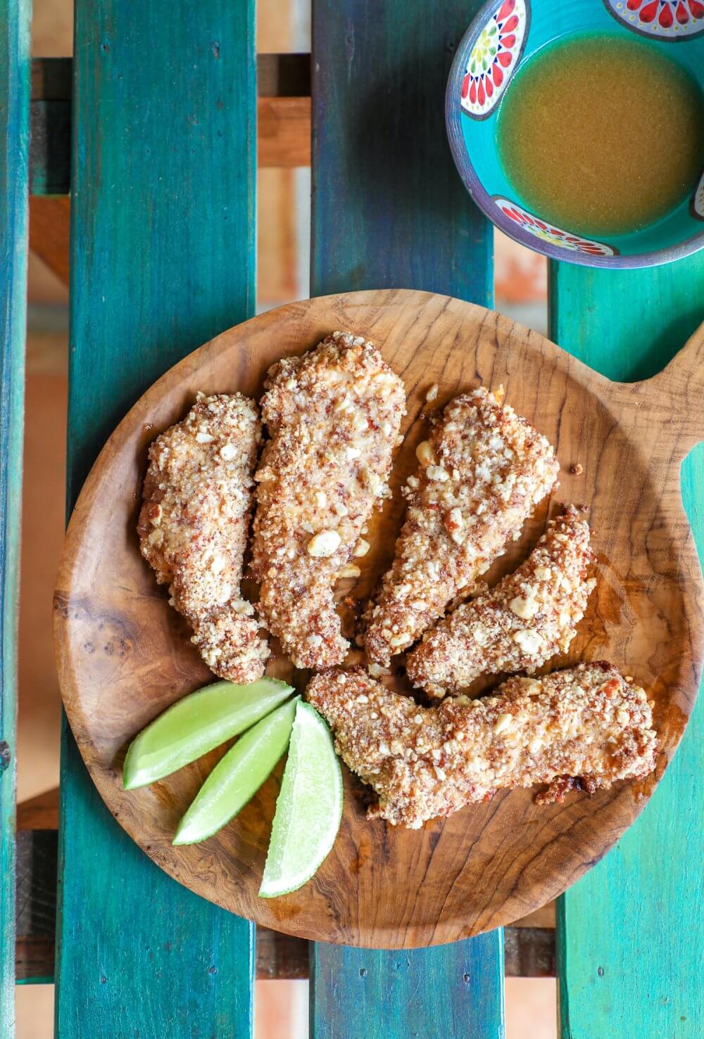Keto Peanut Chicken Tenders on a wooden platter garnished with 3 lime wedges