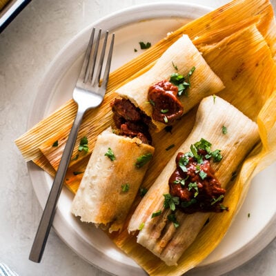 Pork Tamales with red chile sauce on corn husks.