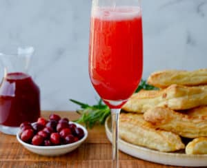 Cranberry Champagne Cocktail in Champagne flute with orange twist and fresh cranberries and pastries in the background