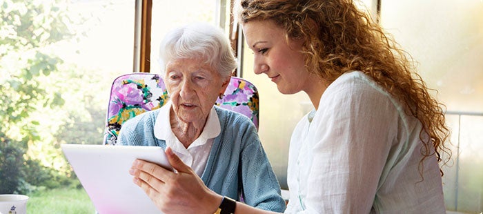 Young woman holding a tablet shows an elderly woman the Centers for Medicare & Medicaid Services new Consumer Alert icon