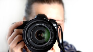 Ein Fotograf h&auml;lt eine Spiegelreflexkamera in seinen H&auml;nden.