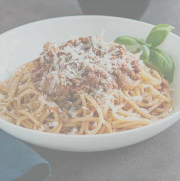white bowl of spaghetti bolognese with a dark overlay