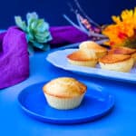 air fryer cornbread muffin on a blue plate with several air fryer cornbread muffins on a white plate