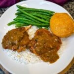 smothered pork chop thighs in a cast iron skillet with gravy